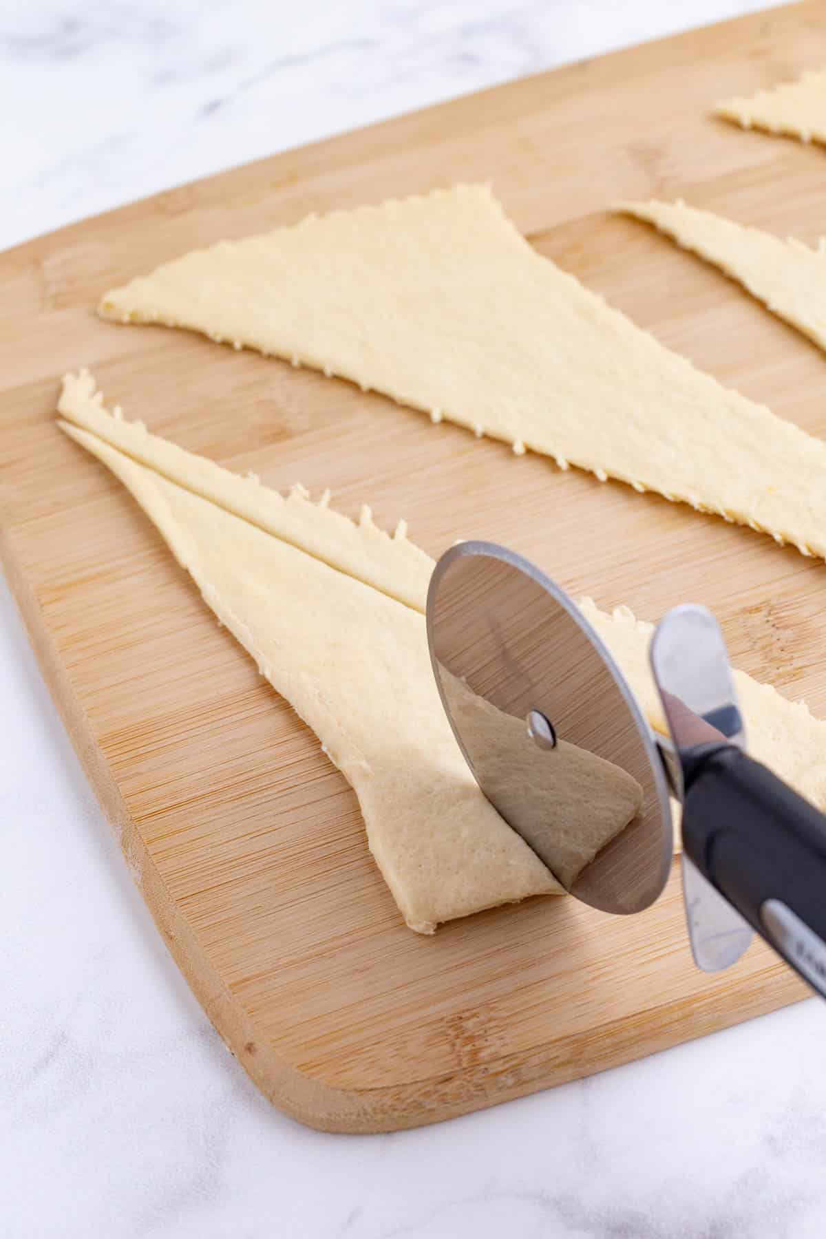 A pizza cutter slices crescent dough.