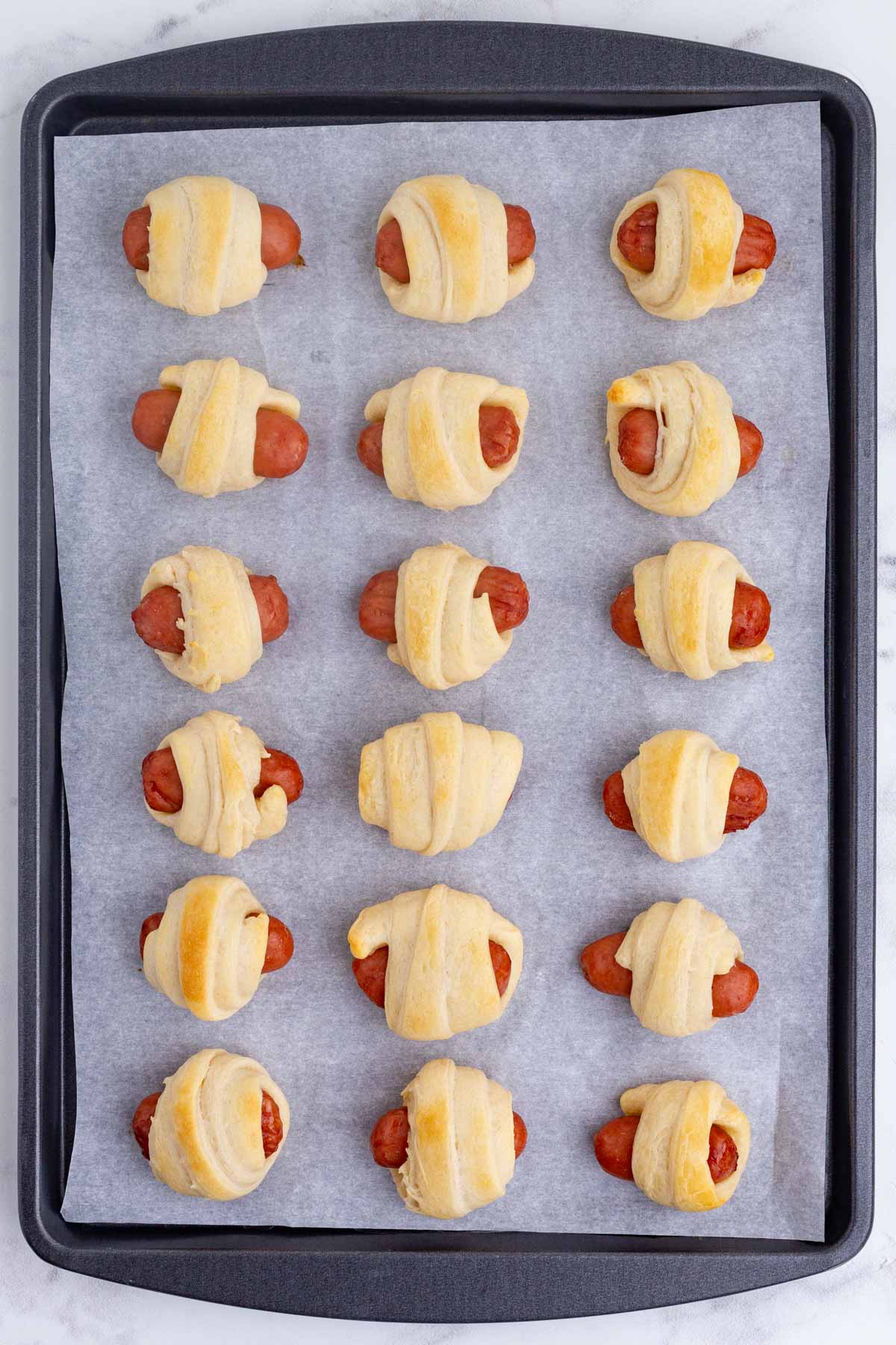 Pigs in a blanket are baked to golden perfection on a baking sheet.
