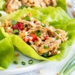 Chicken lettuce wraps with an Asian peanut sauce on a white plate next to green onions.