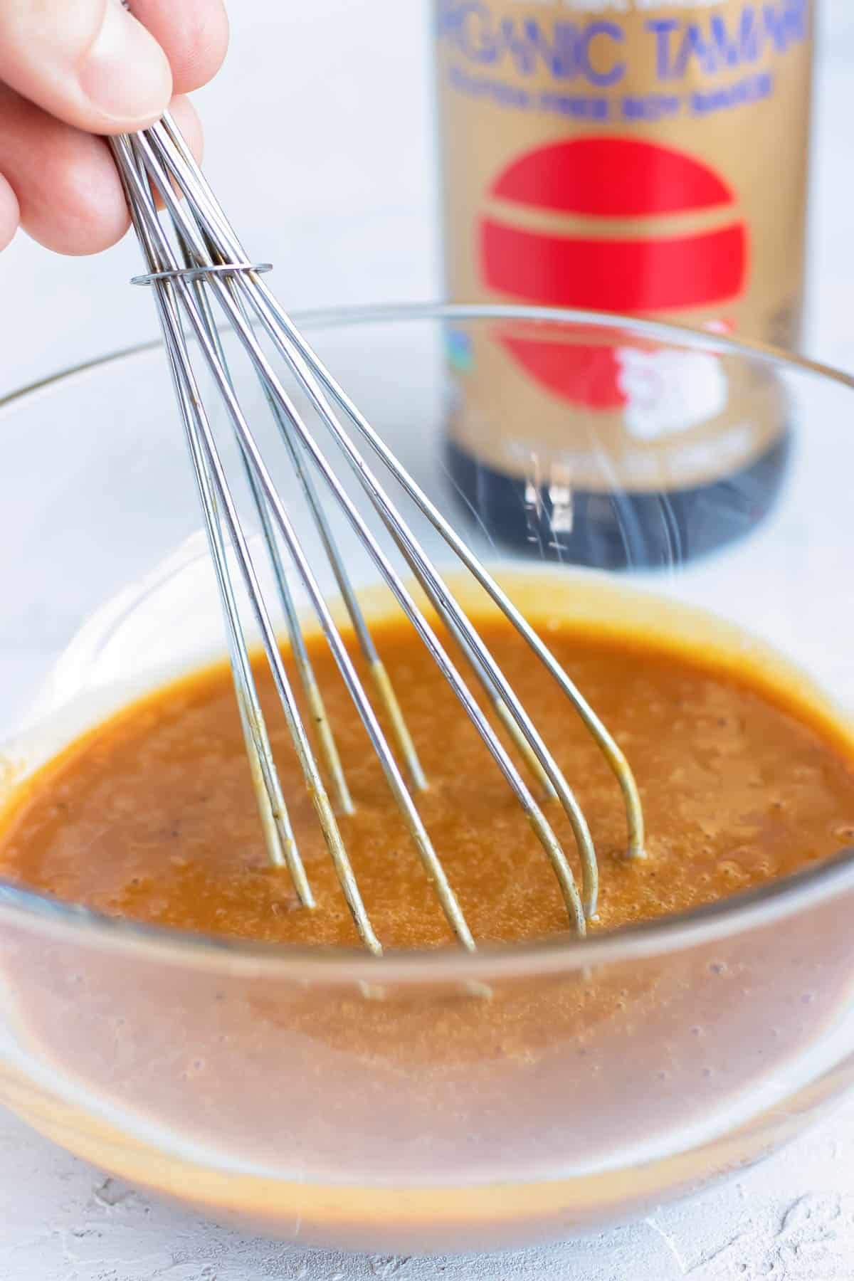 Asian peanut sauce in a clear bowl that is being whisked until smooth.