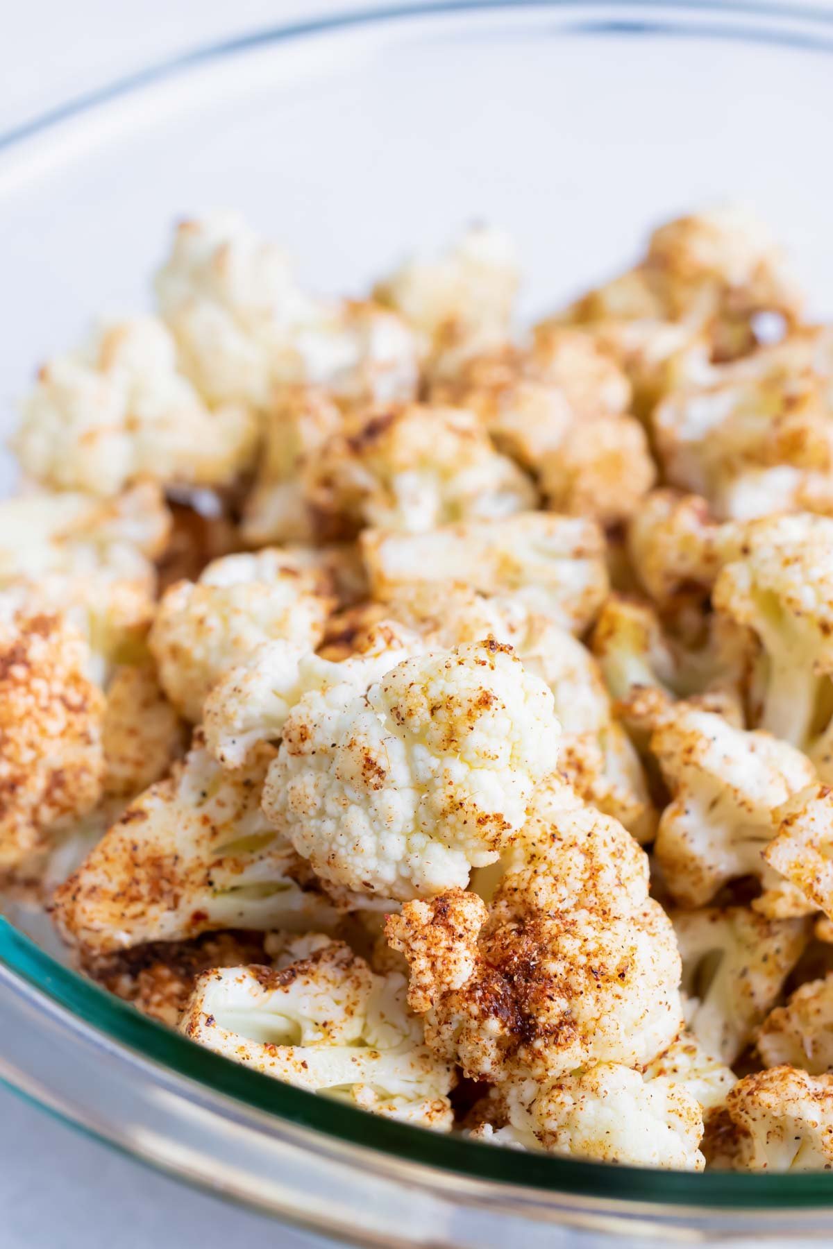 A glass bowl full of cauliflower that has been tossed in a seasoning mix.