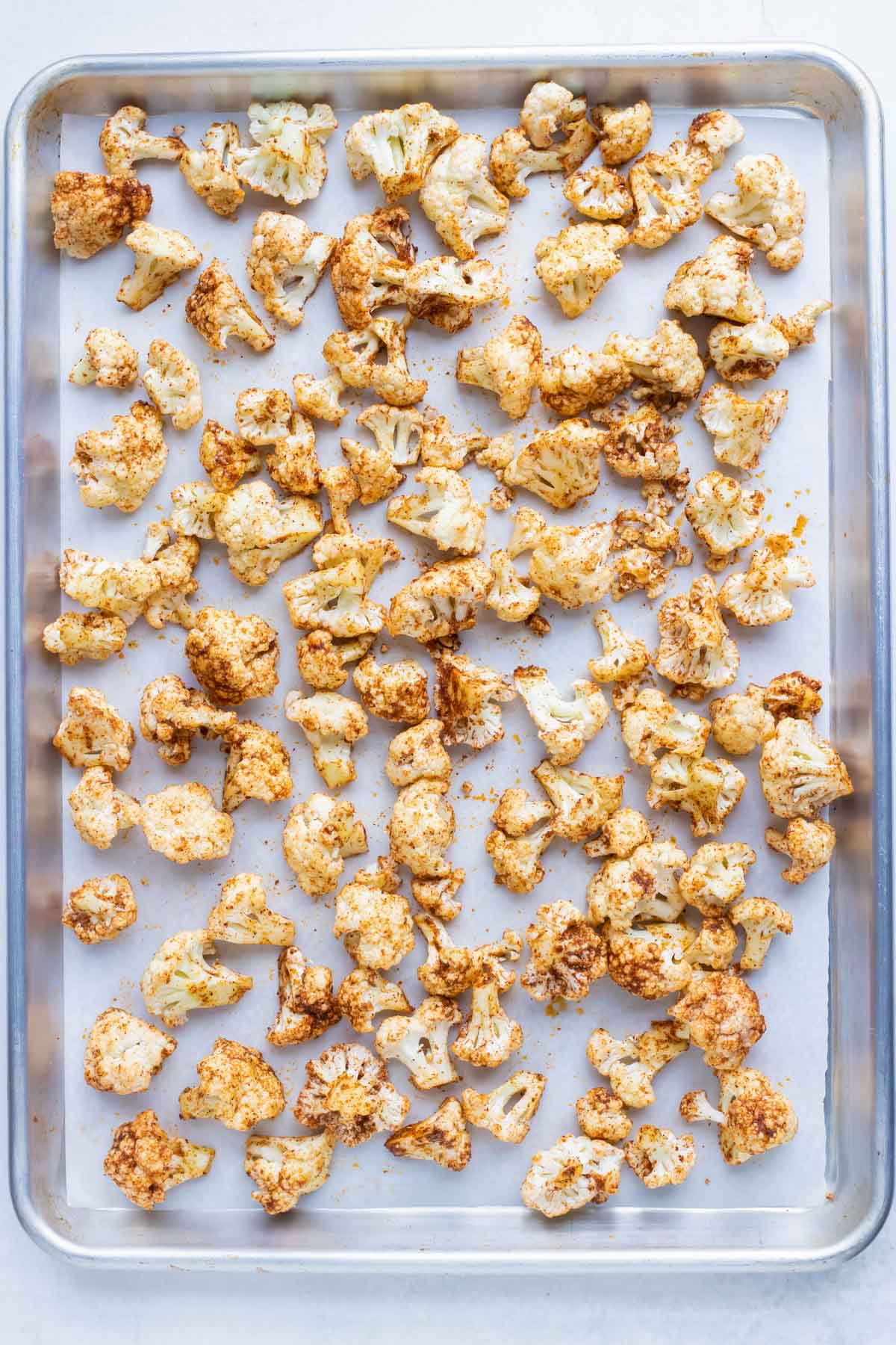 Cauliflower coated in taco seasoning on a baking sheet before roasting in the oven.