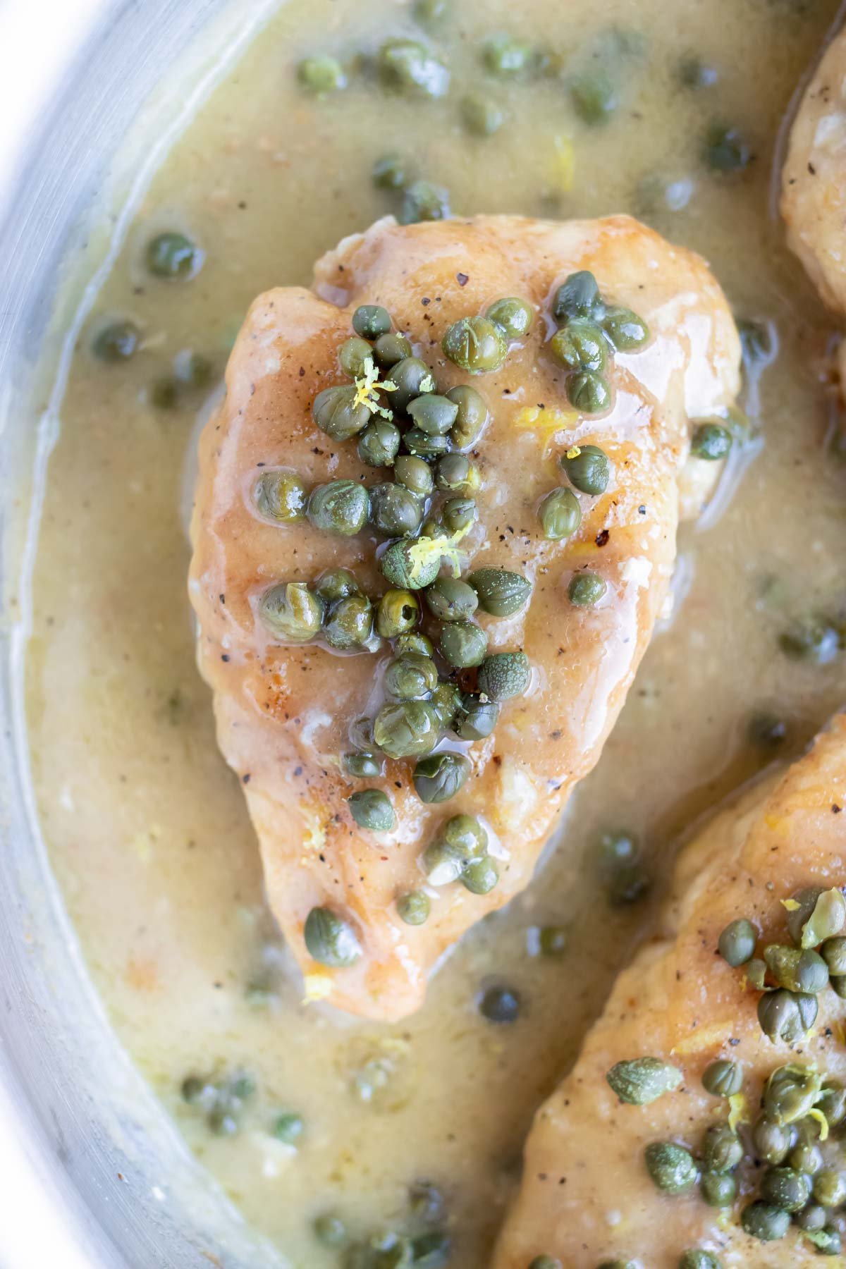 Cooked chicken breast in a skillet with a lemon butter sauce and capers.