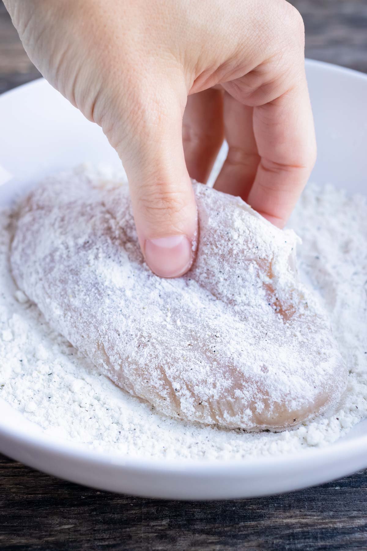 A hand dredging a chicken breast in flour.