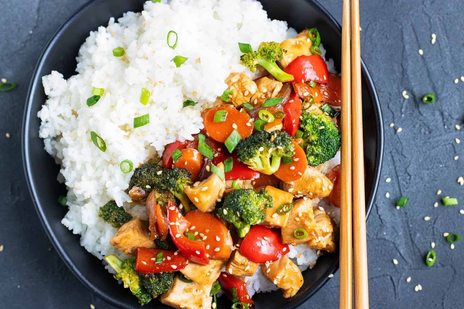 Teriyaki chicken with rice in a black bowl with chopsticks.