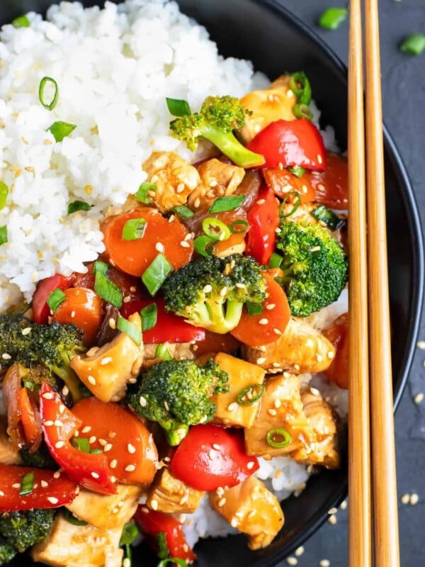 A black bowl full of a teriyaki chicken recipe with wooden chopsticks.