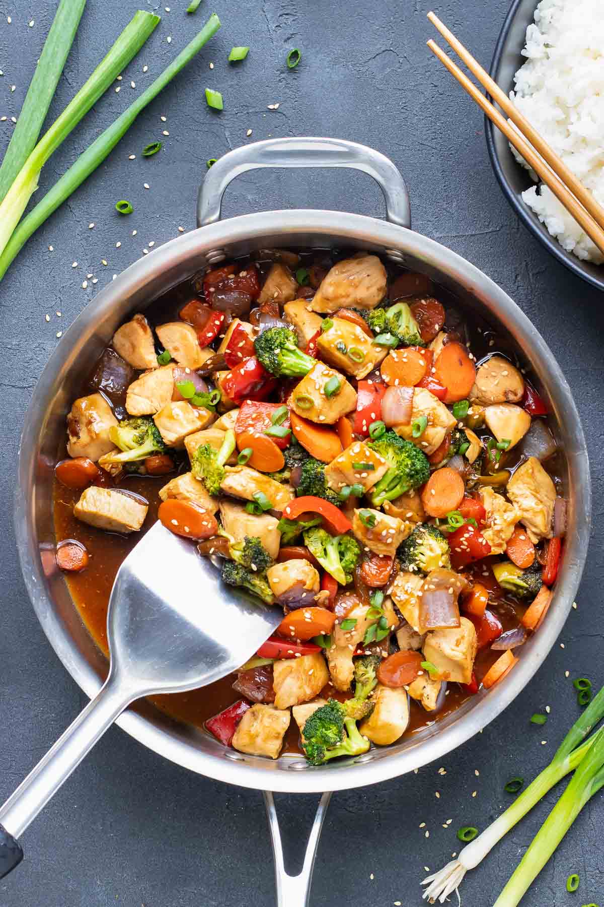 Teriyaki chicken stir fry in a stainless steel skillet with a spatula.