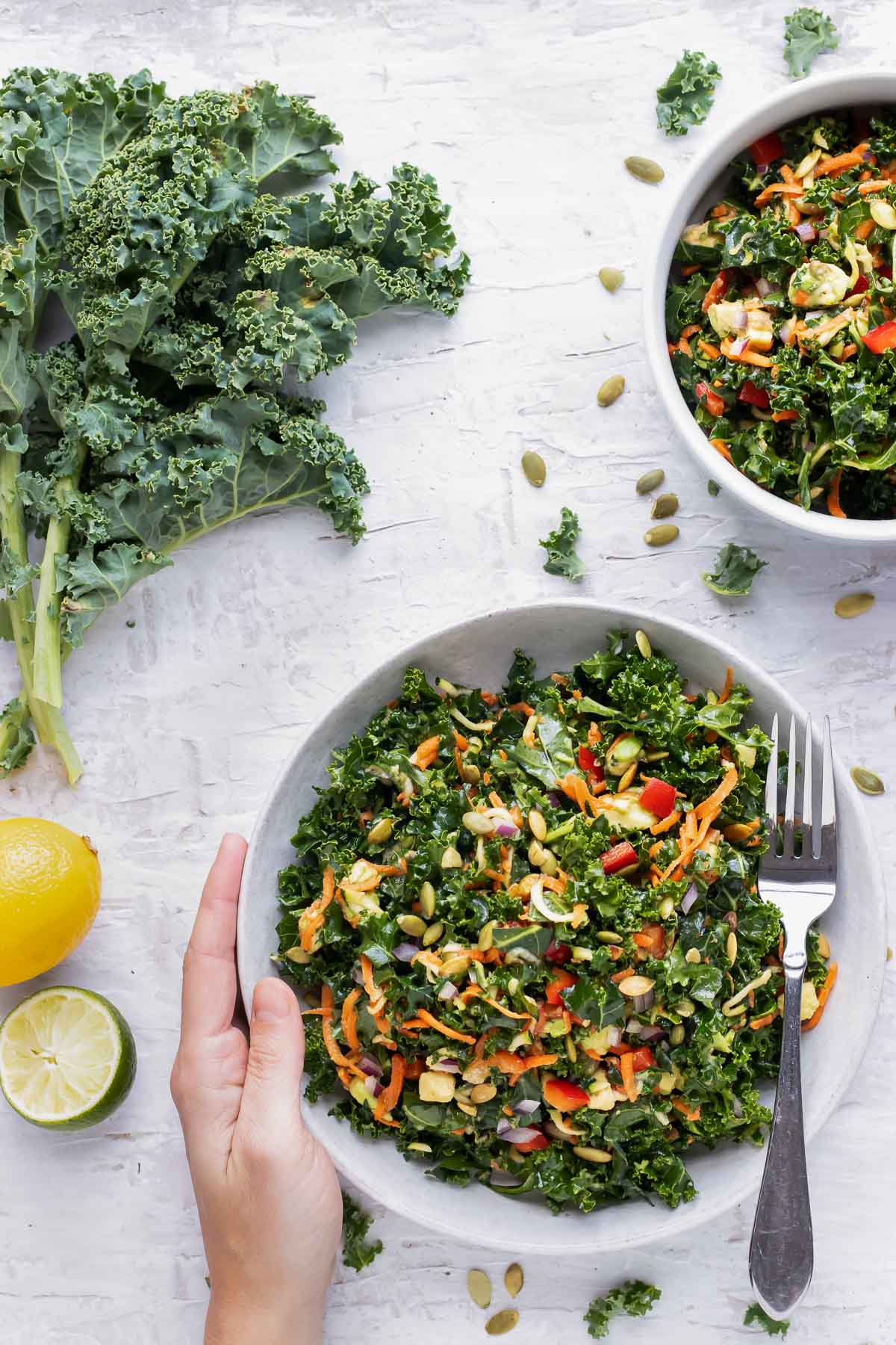 Two salad bowls full of a healthy kale salad recipe with avocado and lemon dressing.