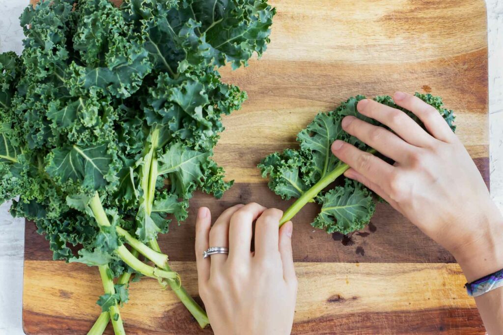 A hand removes the leaves from the rib of the kale.