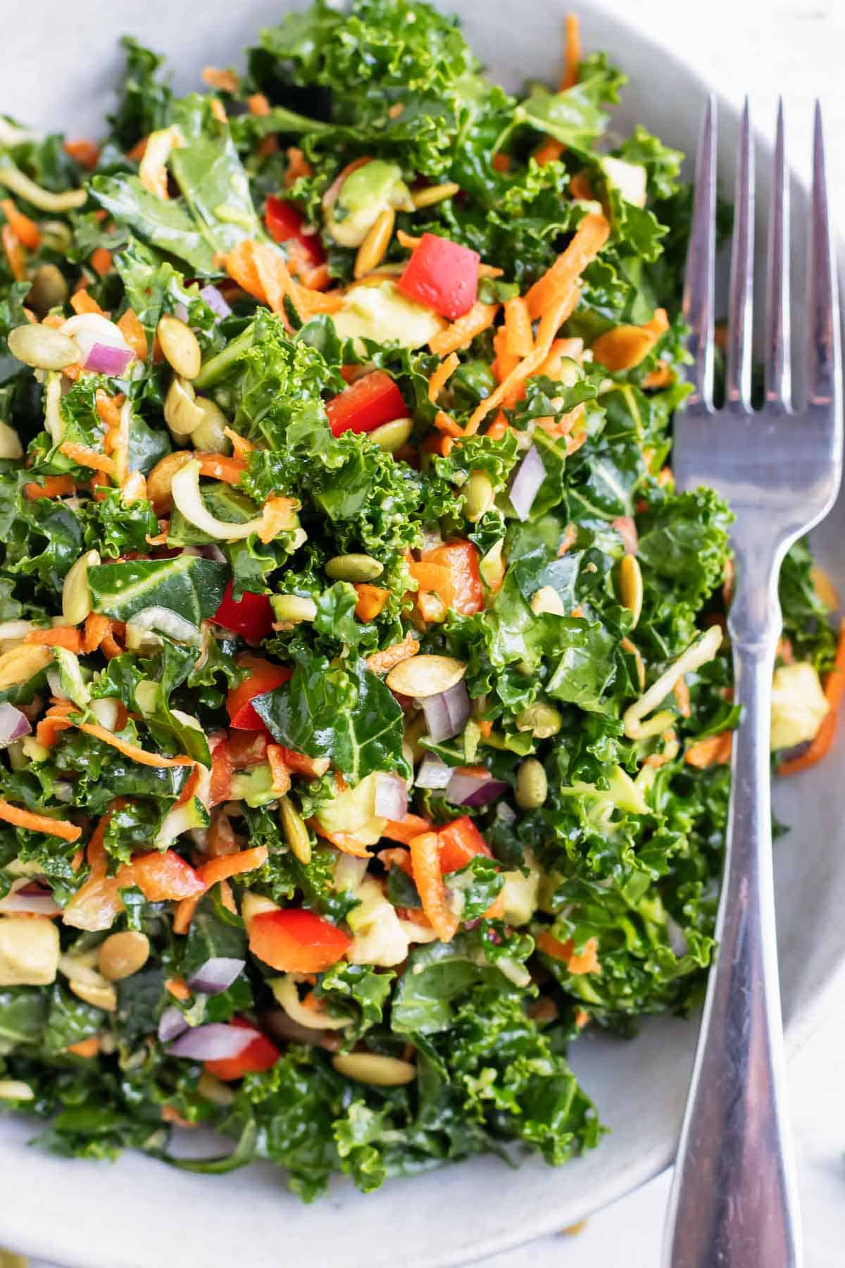 A large white bowl full of kale, avocado, bell pepper, carrots, and a lemon salad dressing.