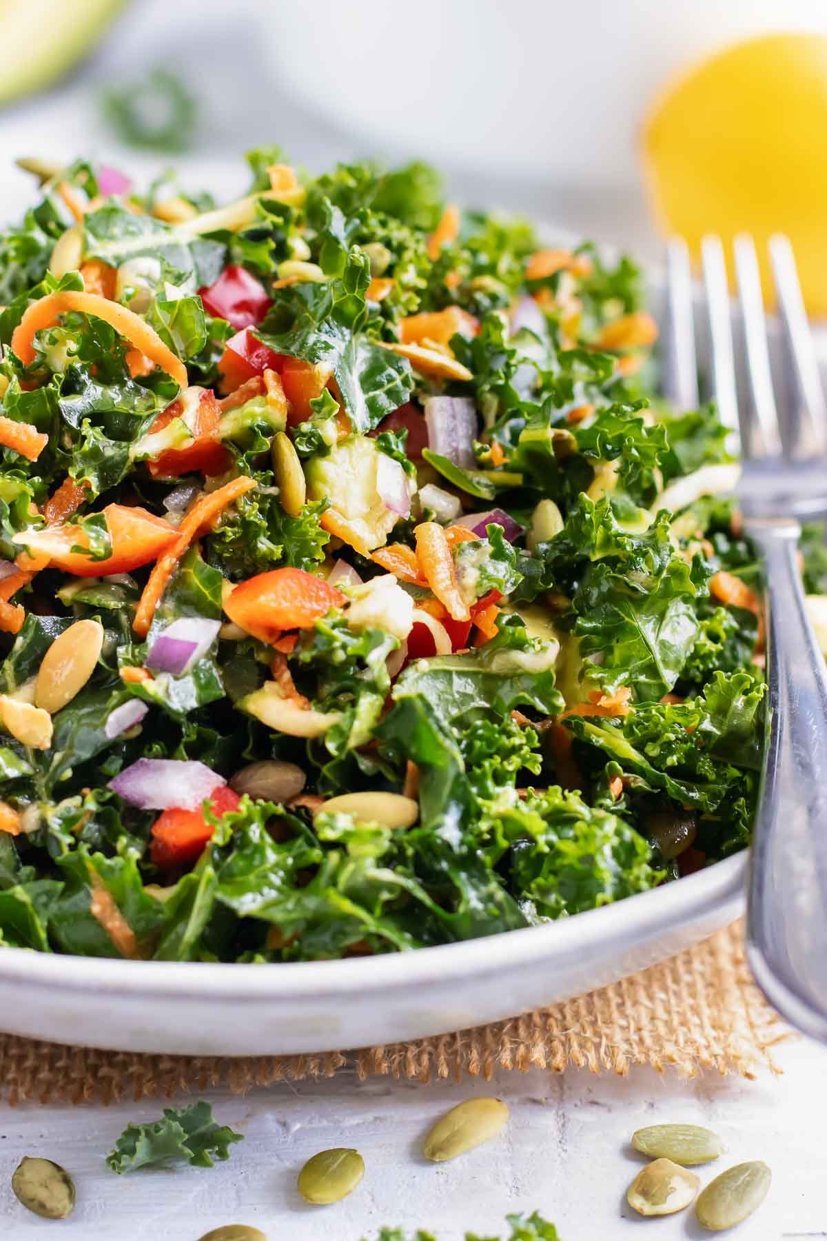 A massaged kale salad with avocado in a white bowl.