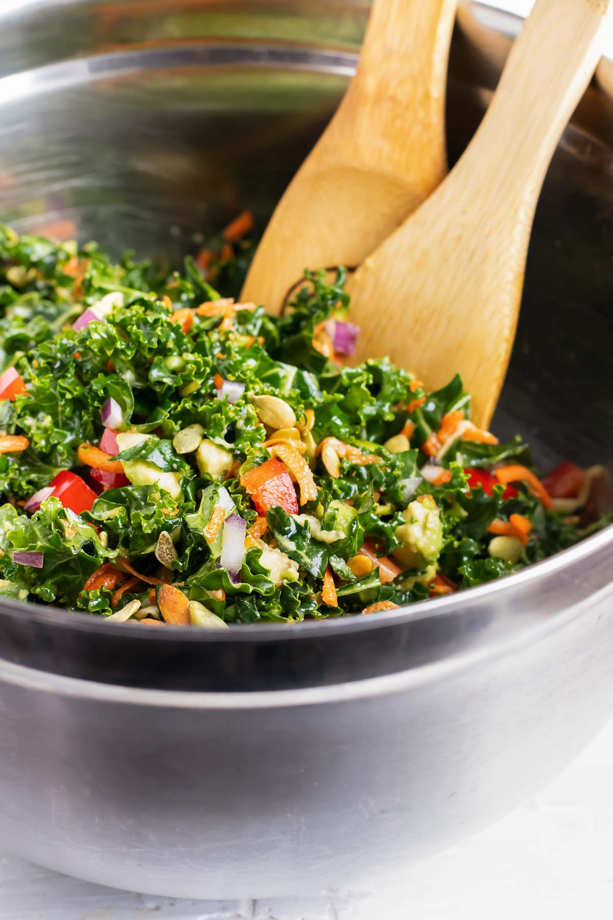 Tossing together a massaged kale salad with wooden tongs in a metal bowl.