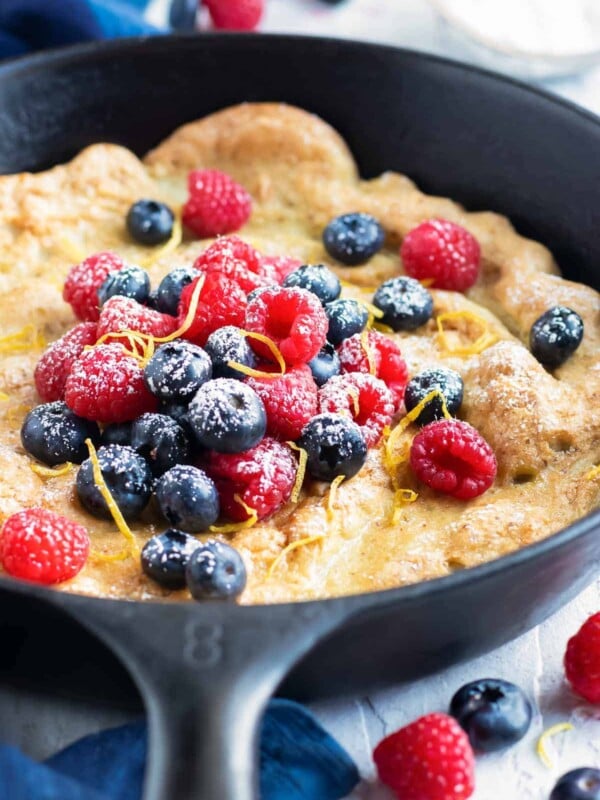 Dutch baby pancake recipe in a cast iron skillet with raspberries and blueberries.