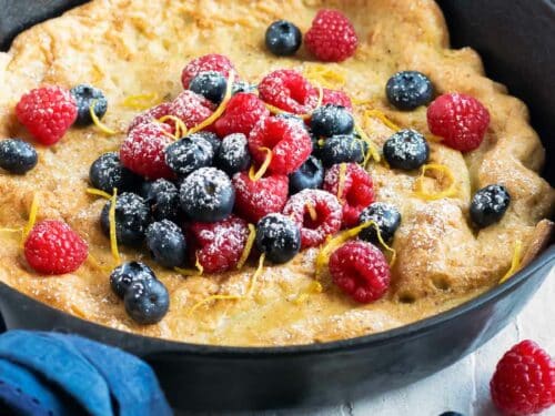 A skillet full of a Dutch baby popover pancake recipe surrounded by fresh berries and lemons.