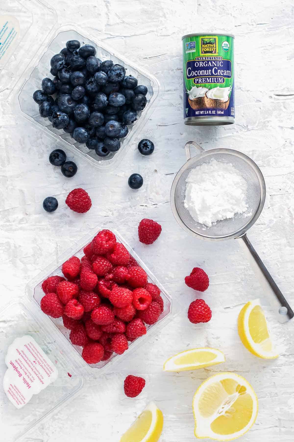Blueberries, raspberries, coconut cream, powdered sugar, and fresh lemons and topping ideas for pancakes.