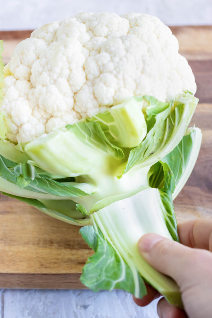 Trimming and removing the green leaves from a head of cauliflower.