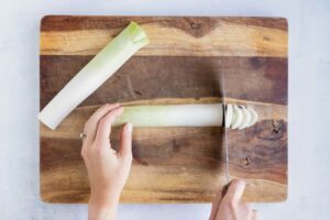 A cutting board with a fresh leek on it and cutting it into thin slices.