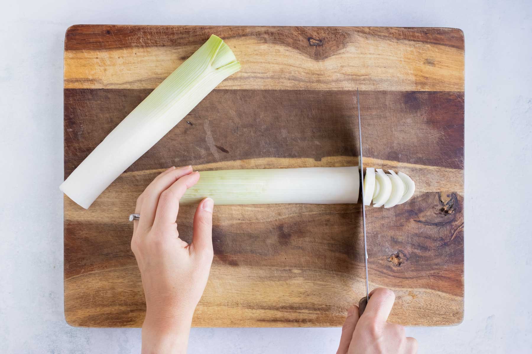 A cutting board with a fresh leek on it and cutting it into thin slices on a wooden cutting board.