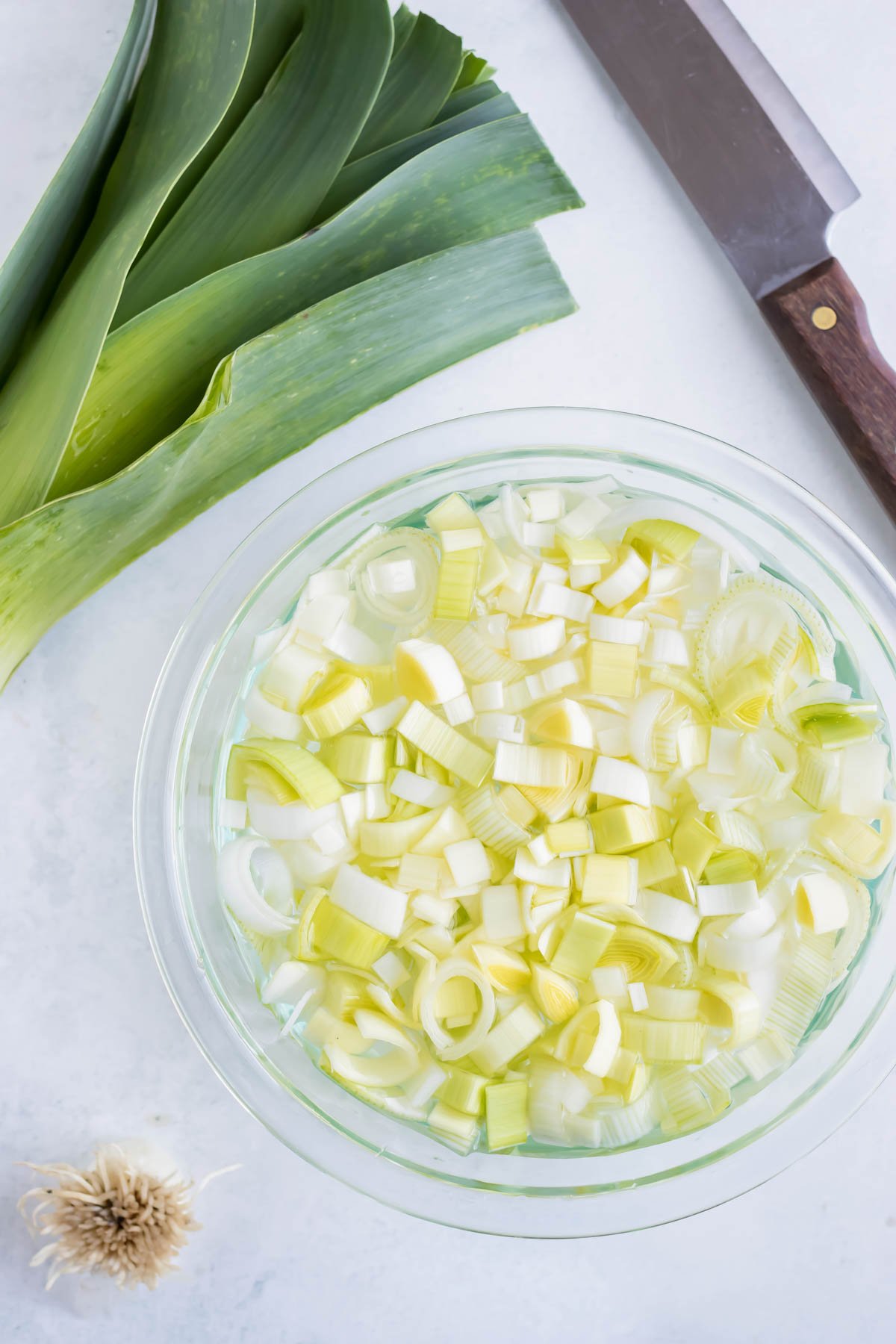 Fresh leeks that have been cut and are being cleaned in a bowl of water.