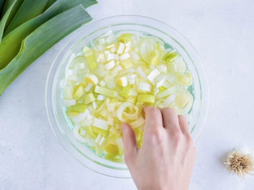 A hand picking up sliced leeks out of a bowl of water after cleaning them.
