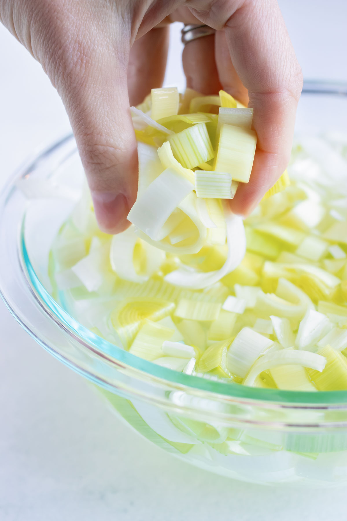 A hand picking up sliced leeks out of a bowl of water.