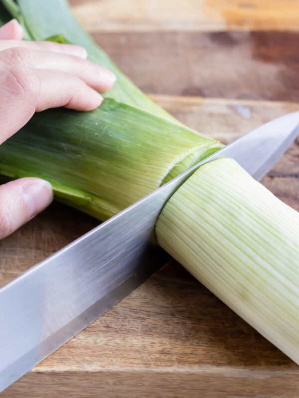 An image showing how to cut fresh leeks to use the white part for soup and discard the green part.