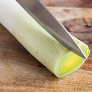 A fresh leek that is being cut down the middle lengthwise.
