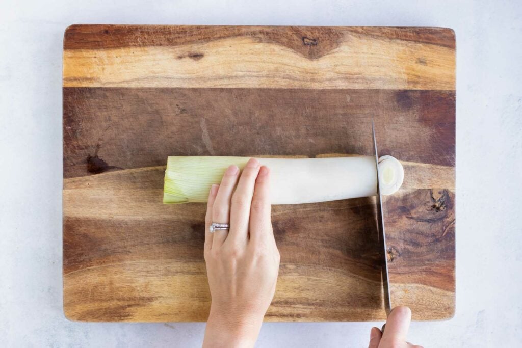 A cutting board with a fresh leek on it and cutting it into thin slices.