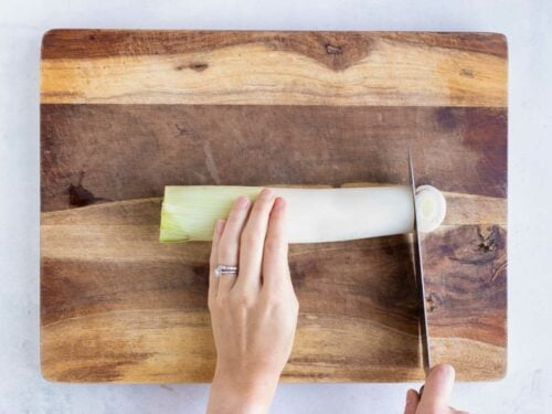 A cutting board with a fresh leek on it and cutting it into thin slices.