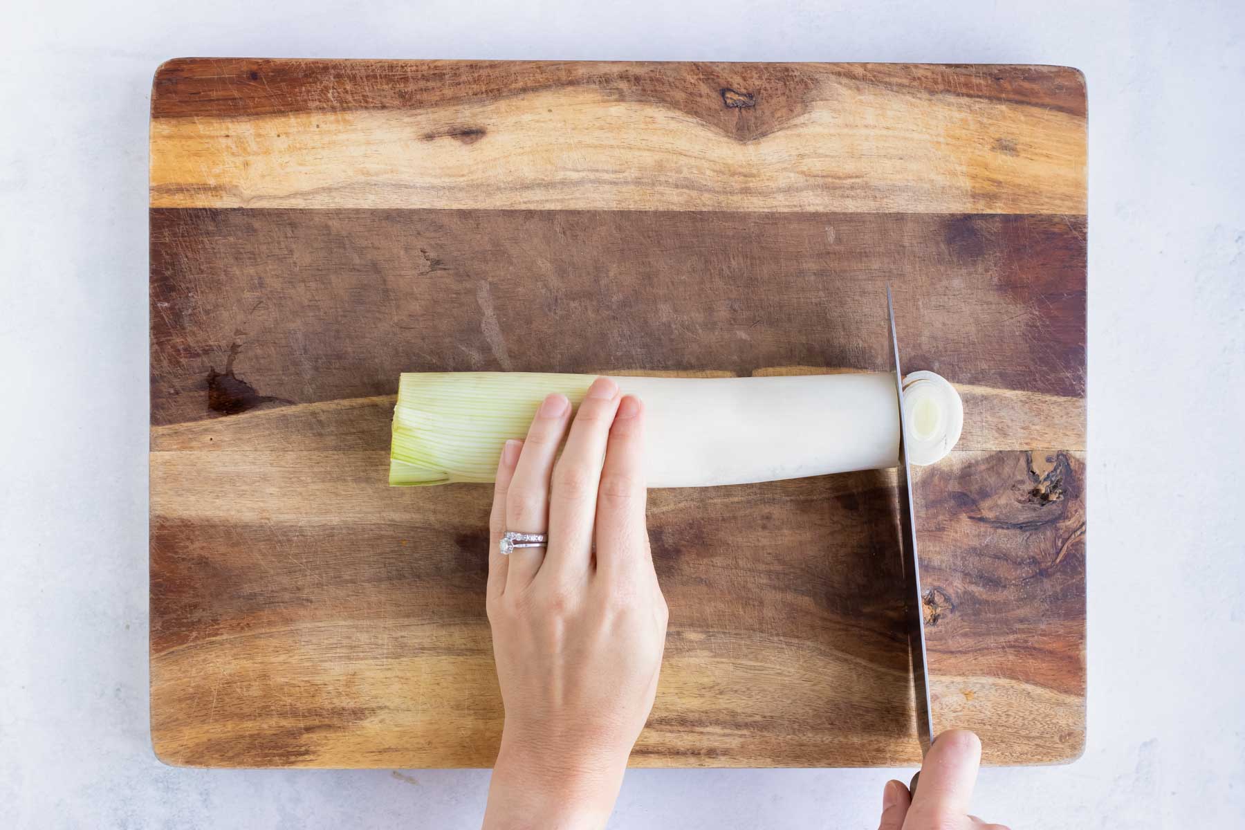 A wooden cutting board with a fresh leek on it and cutting it into thin slices.