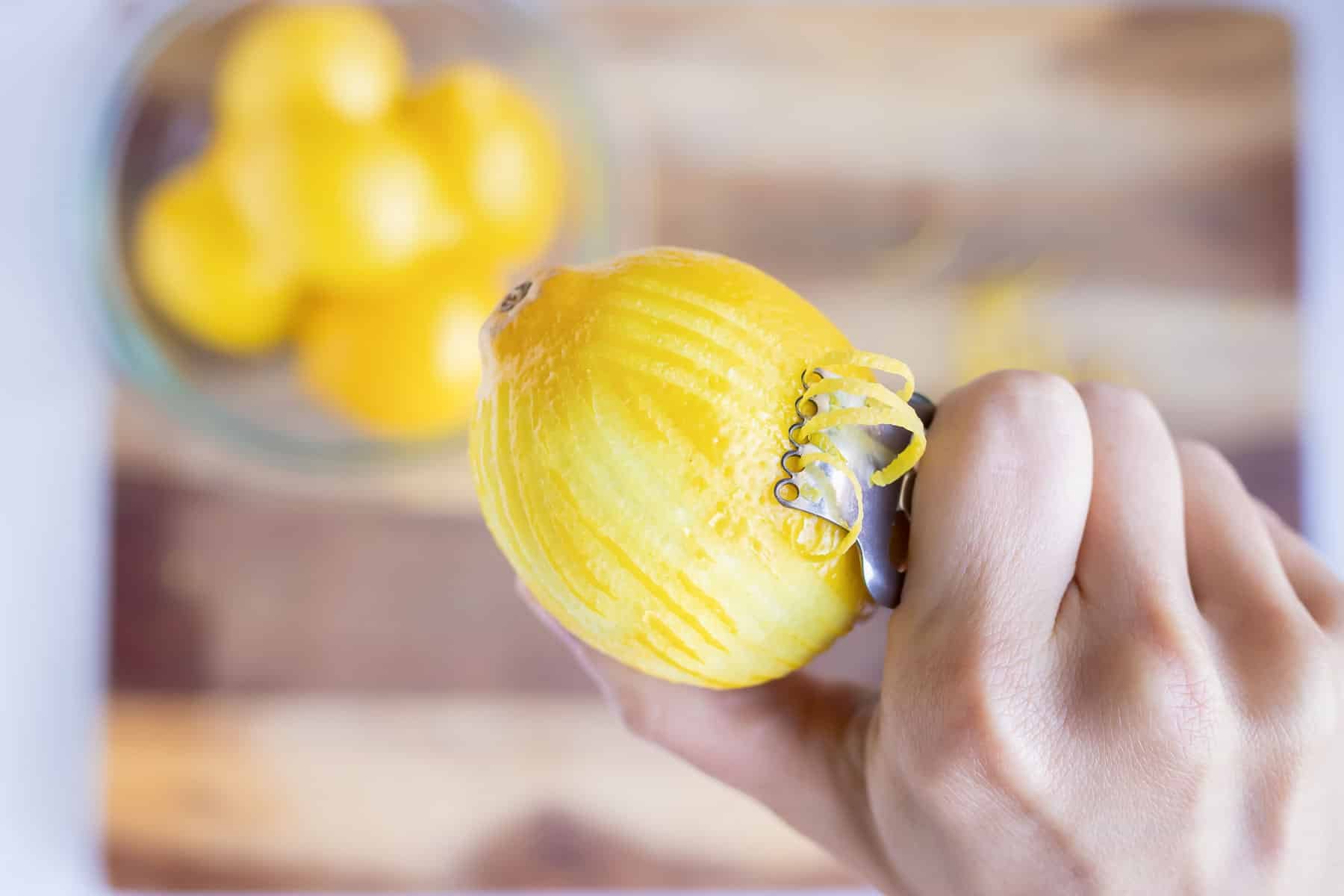 A hand with a citrus zester showing how to zest a lemon.