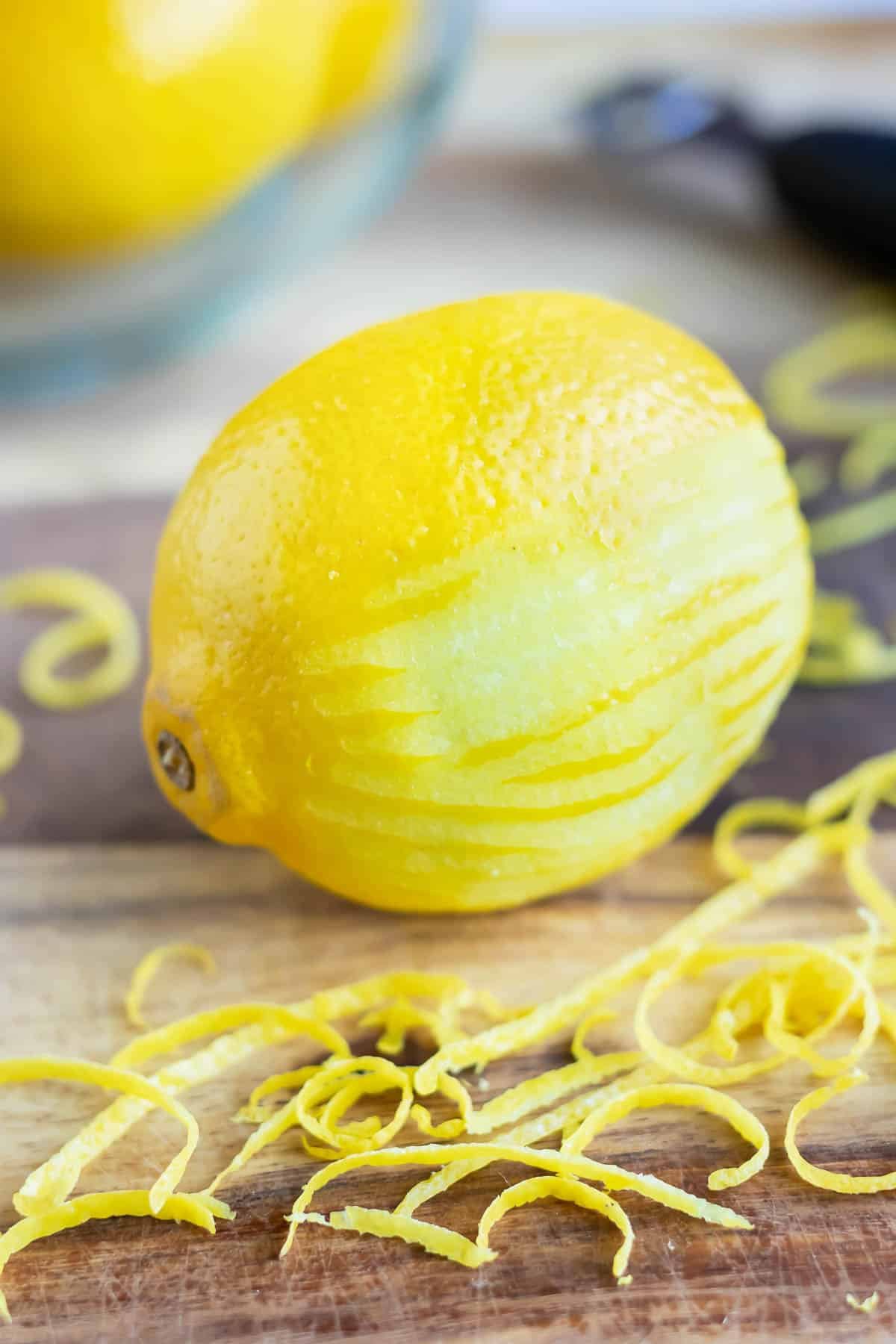 A lemon that has been partially zested on a cutting board with lemon zest around it.
