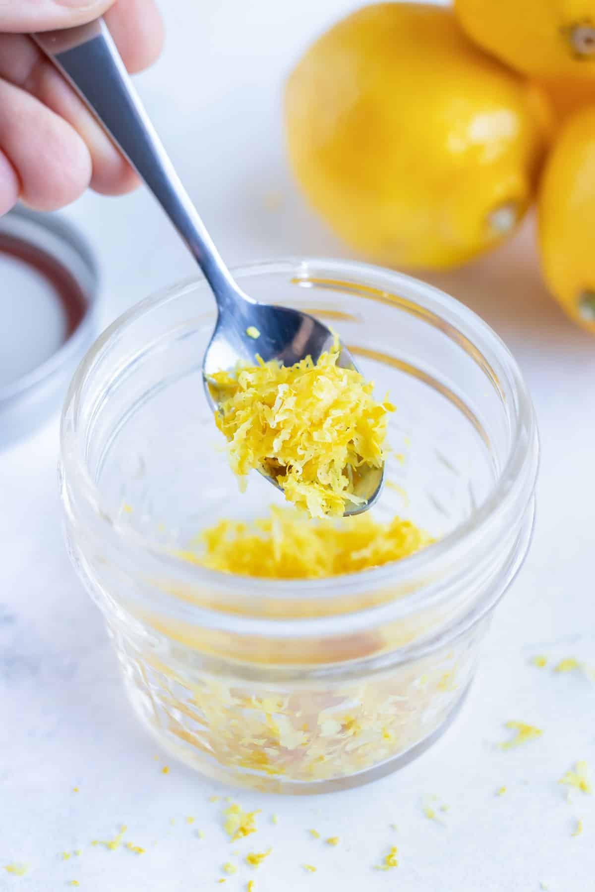 A glass jar full of lemon zest and a silver spoon scooping some out.
