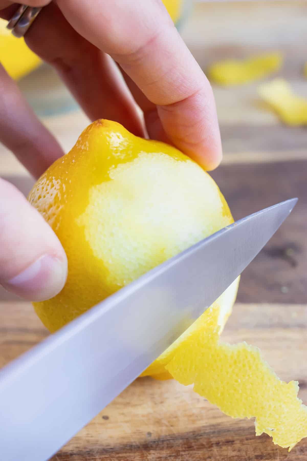A hand with a paring knife carefully showing how to zest a lemon.