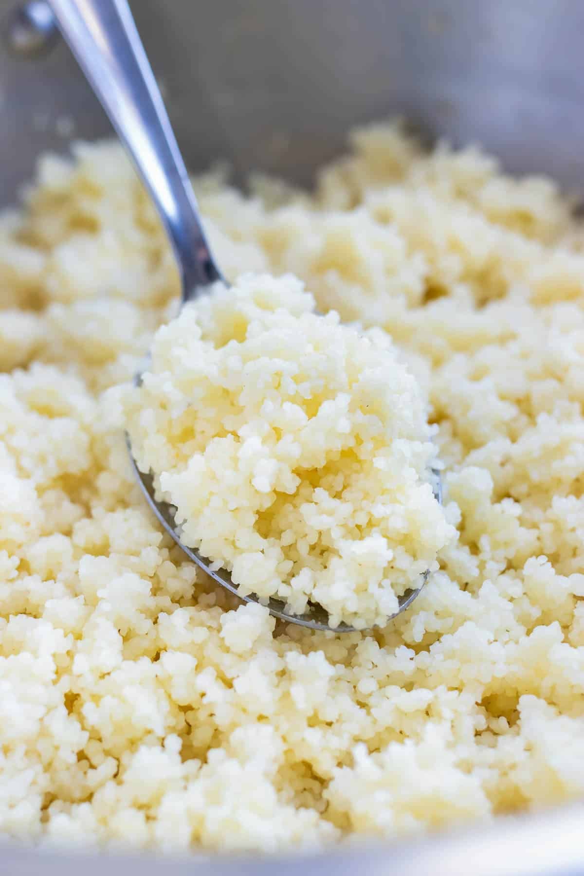 A metal spoon fluffing up Instant couscous in a stainless steel pot.