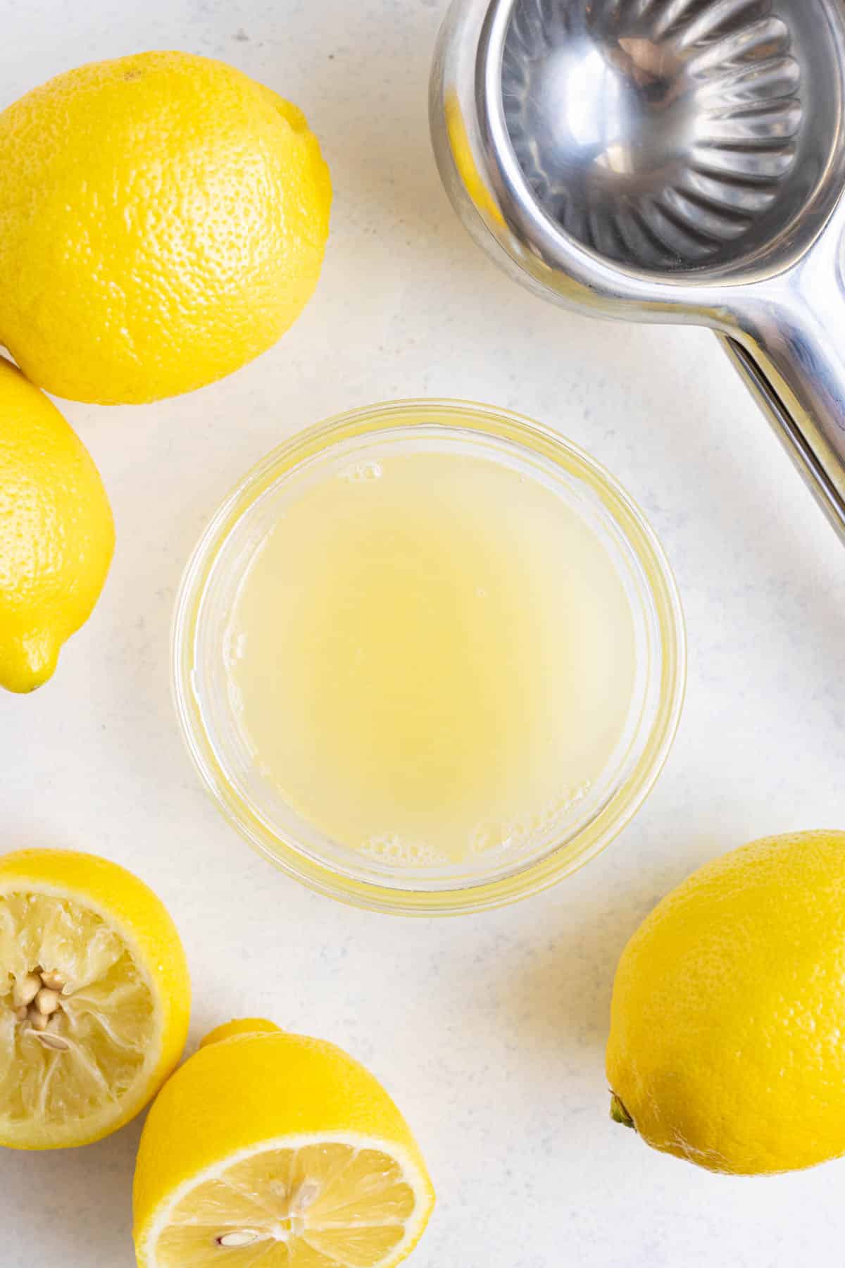 Fresh lemon juice in a small glass bowl with lemons in the background on the countertop.