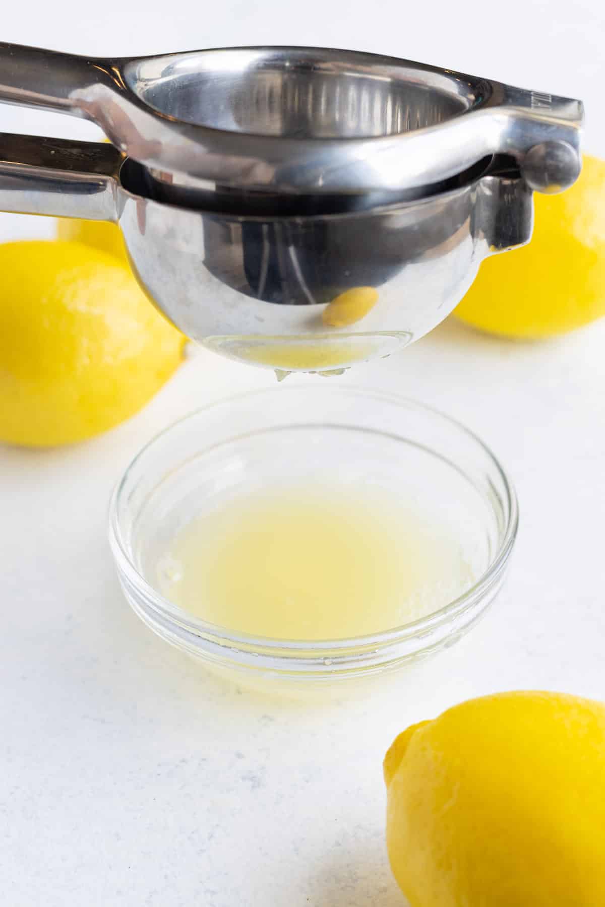 Lemon juice being squeezed into a small glass bowl by a citrus juicer.