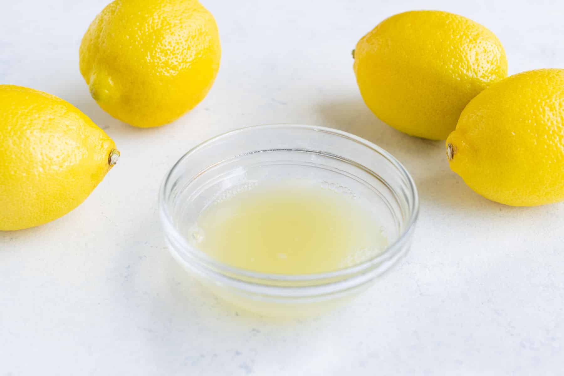 Fresh lemon juice in a small glass bowl with lemons in the background on the countertop.