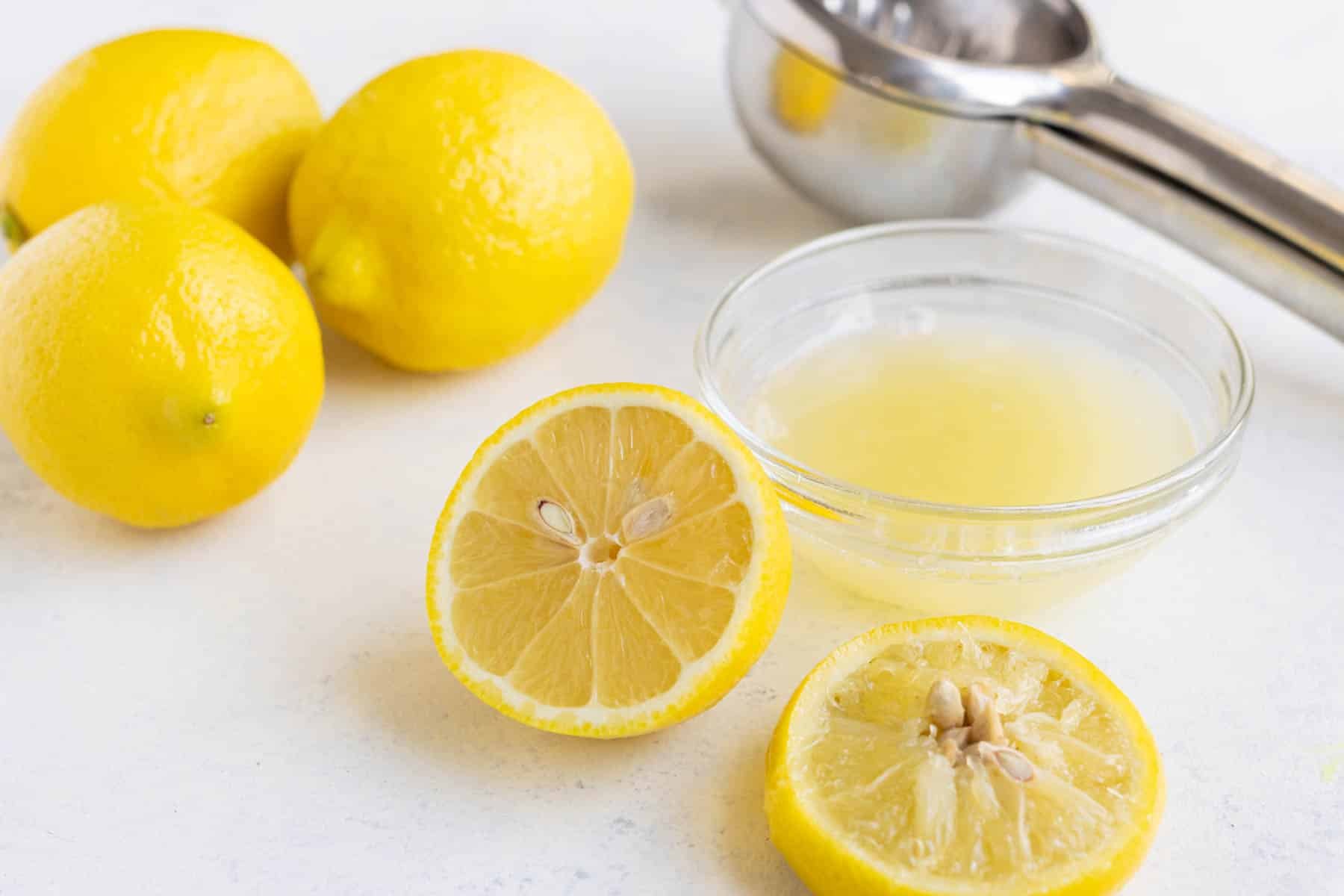 Fresh lemon juice in a small glass bowl with lemons in the background on the countertop.