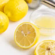 Fresh lemon juice in a small glass bowl with lemons in the background on the countertop.