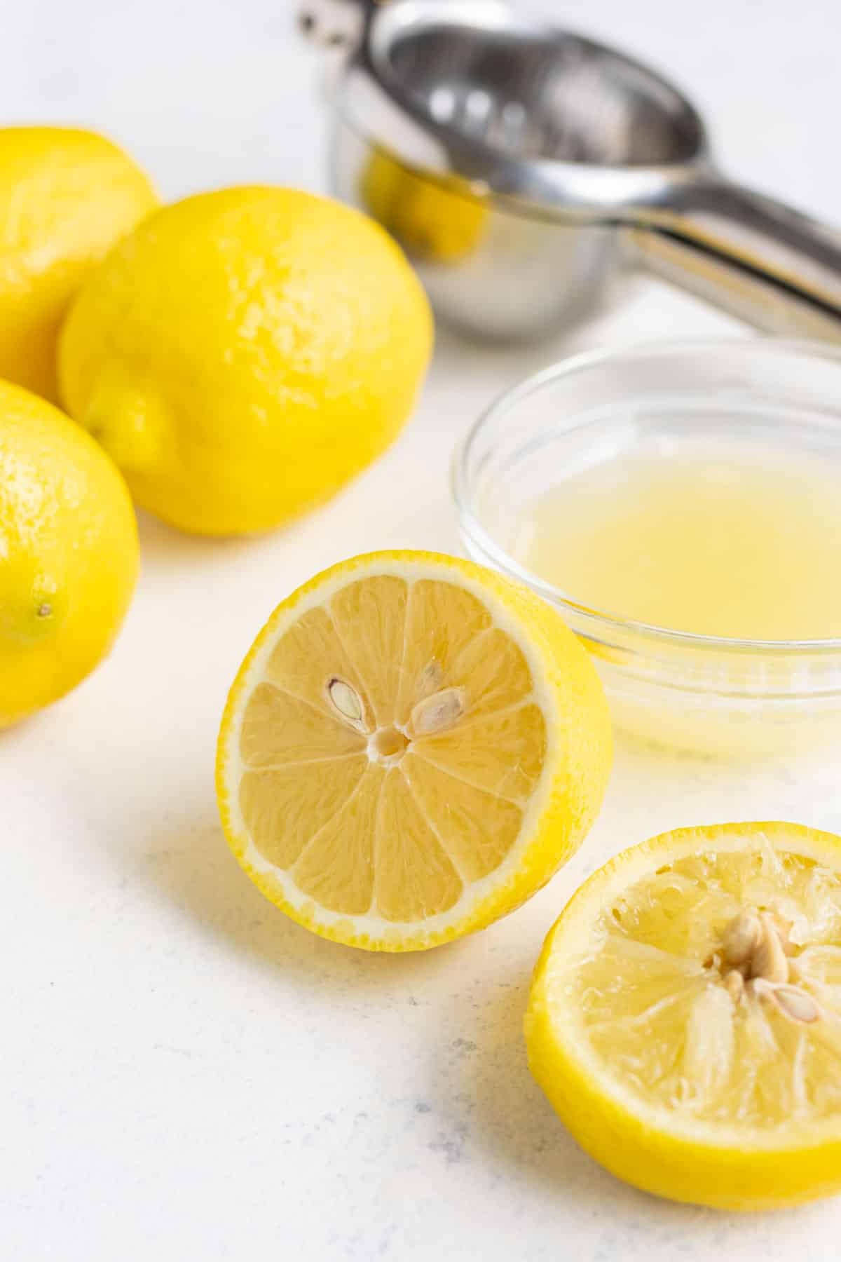 Fresh lemon juice in a small glass bowl with lemons in the background on the countertop.