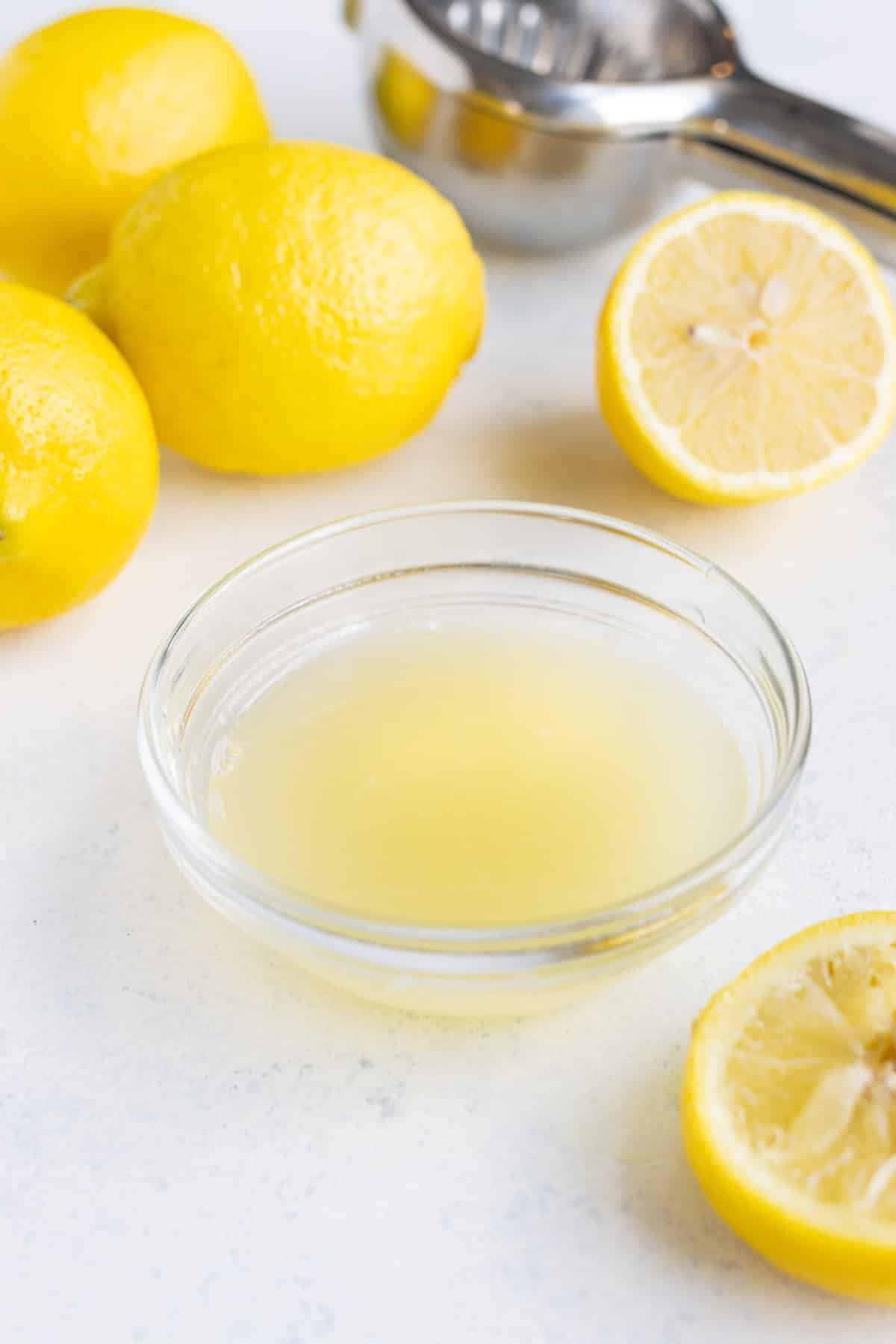 Fresh lemon juice in a small glass bowl with lemons in the background on the countertop.