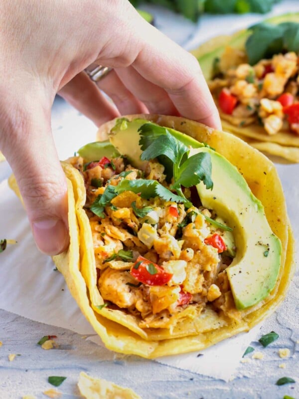 A hand picking up a migas taco from a white table.