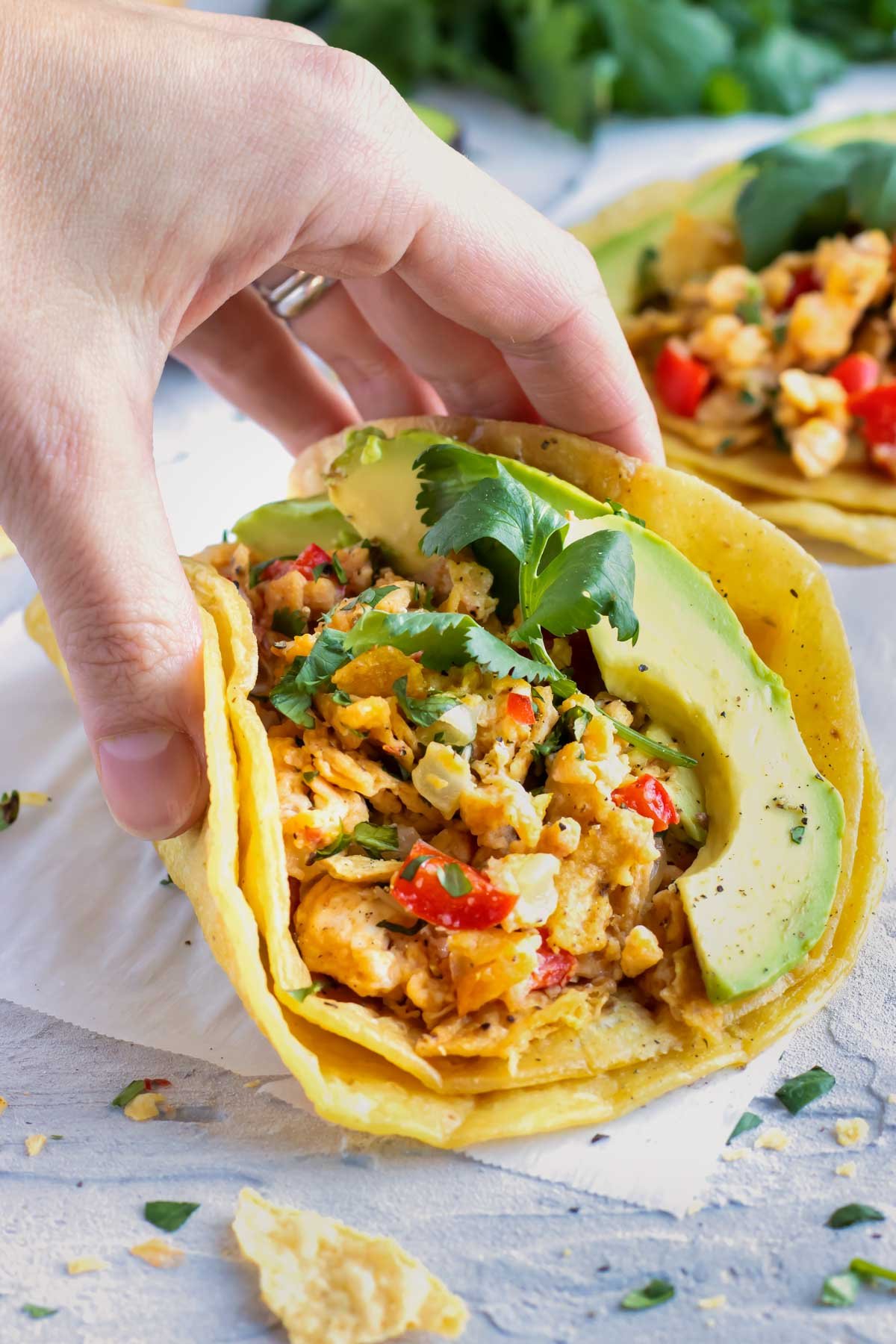 A hand picking up a migas taco from a white table.