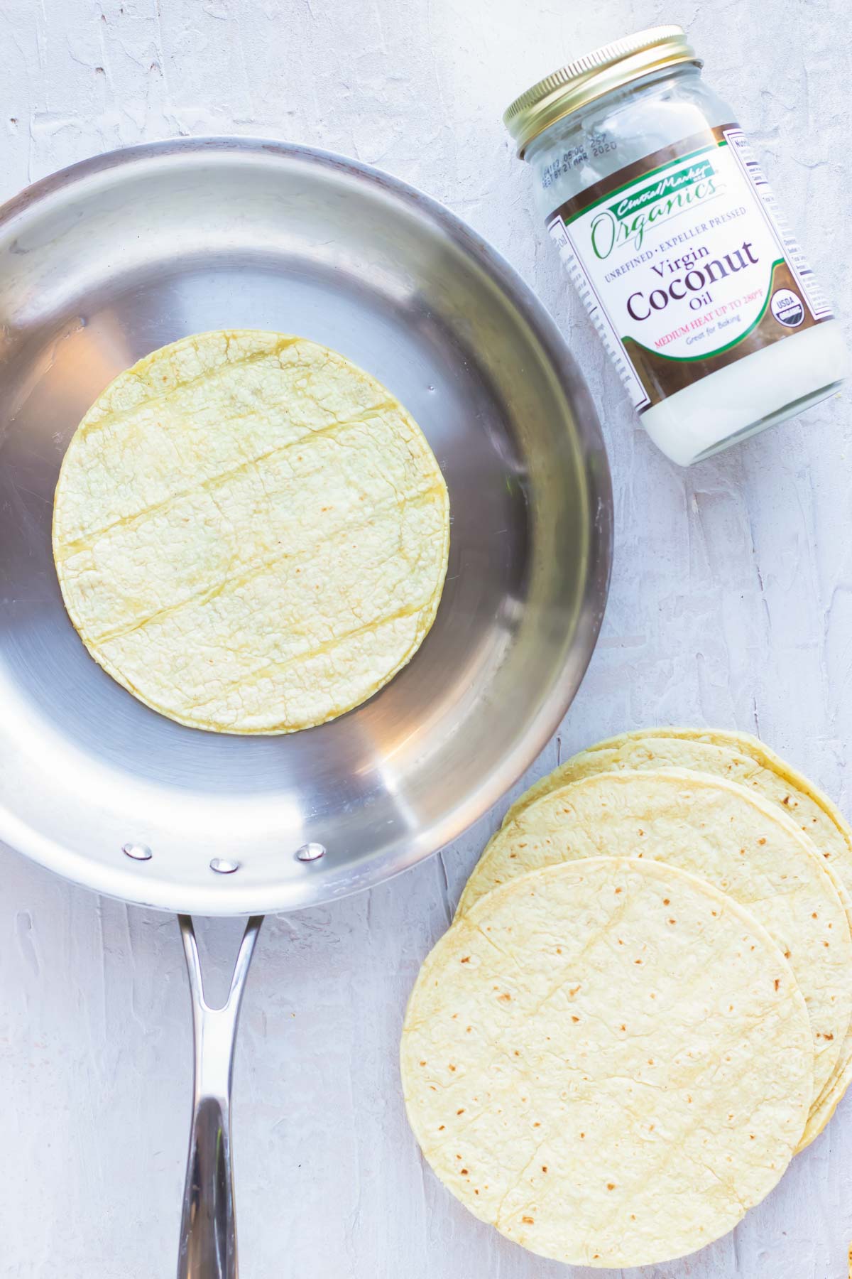 A corn tortilla being heated up with coconut oil in a skillet.