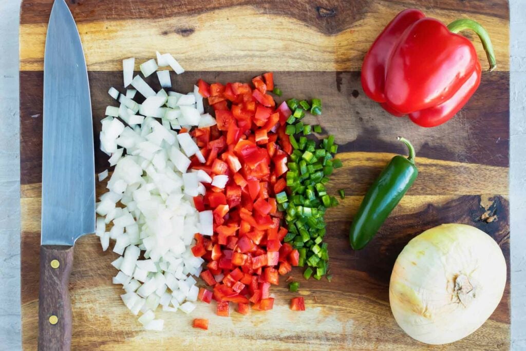 Finely diced onion, red bell pepper, and jalapeno on a white cutting board for an easy Tex-Mex breakfast taco recipe.