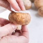 Wiping a whole mushroom with a paper towel.