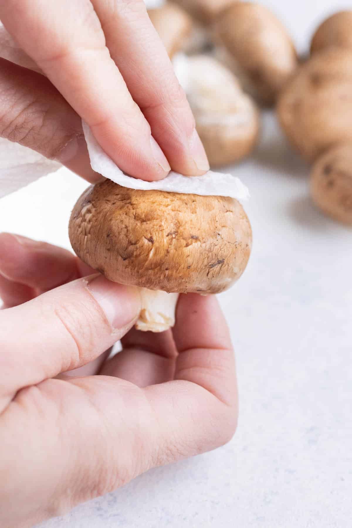 Wiping a whole mushroom with a paper towel.