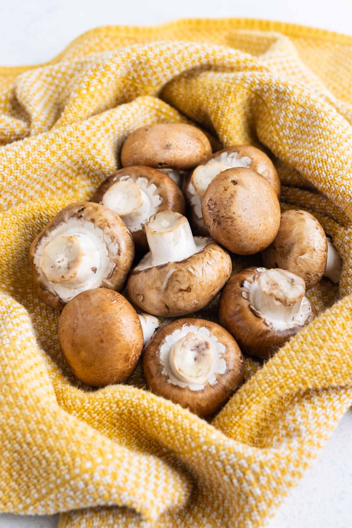 Whole mushrooms surrounded with a yellow kitchen towel.