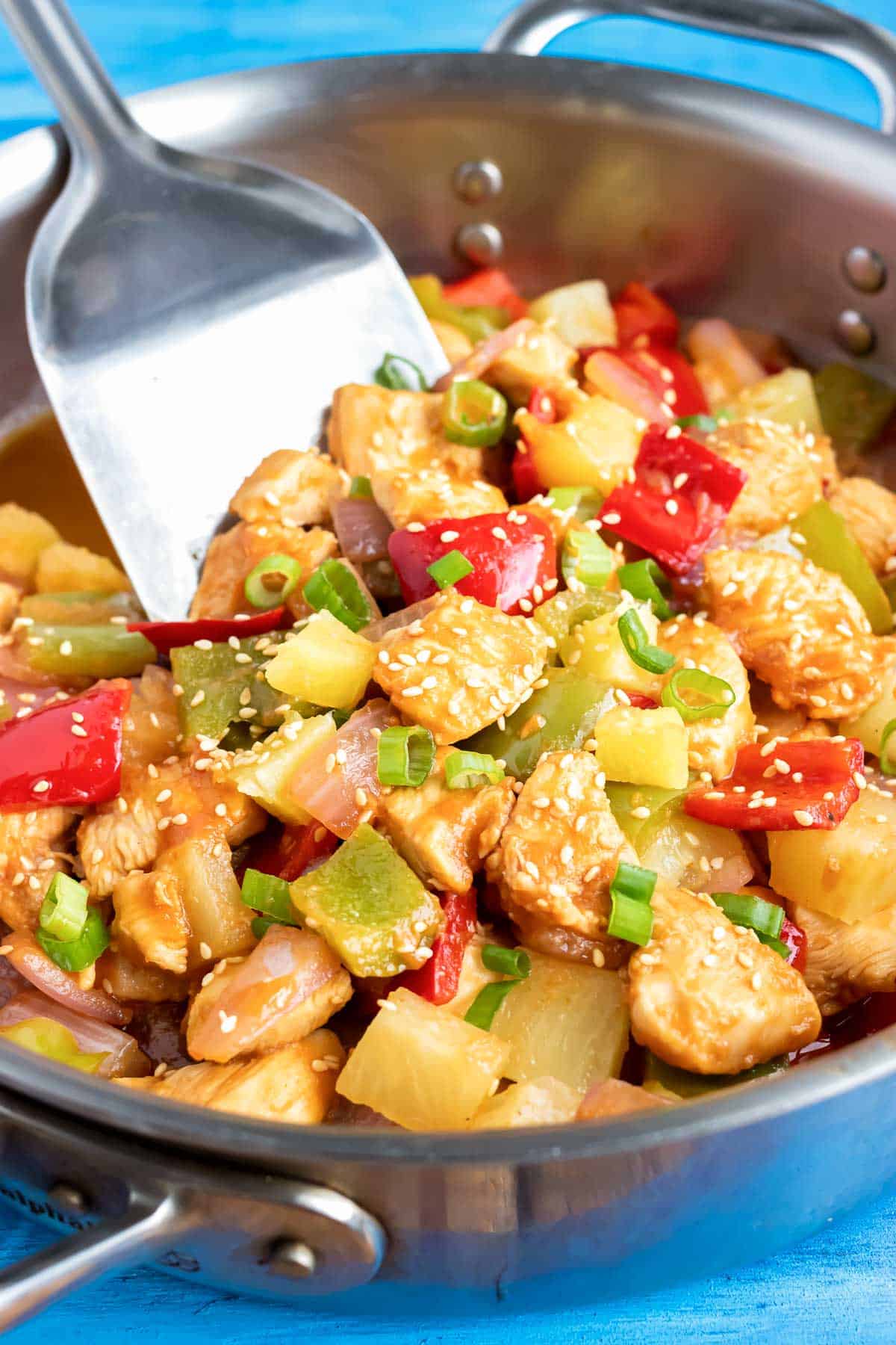 A skillet full of cubed chicken and vegetables in a sticky pineapple sauce.